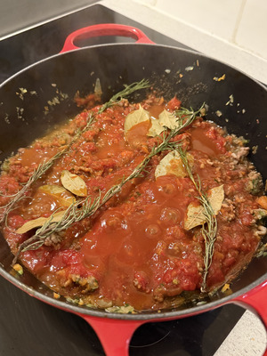 Adding tomato purée, rosemary, and bay leaves to ragù